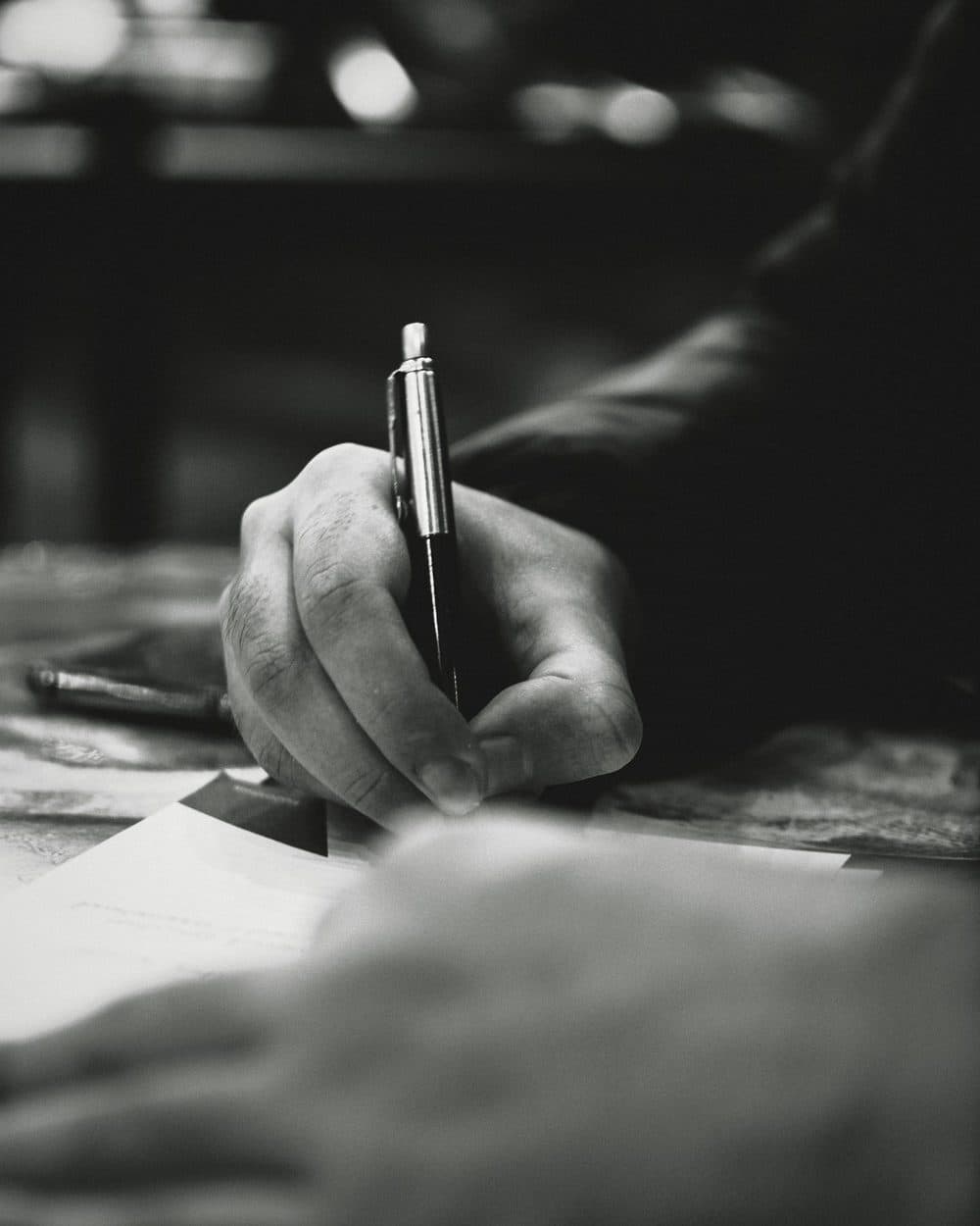 A hand signing a document with a pen, in black and white.