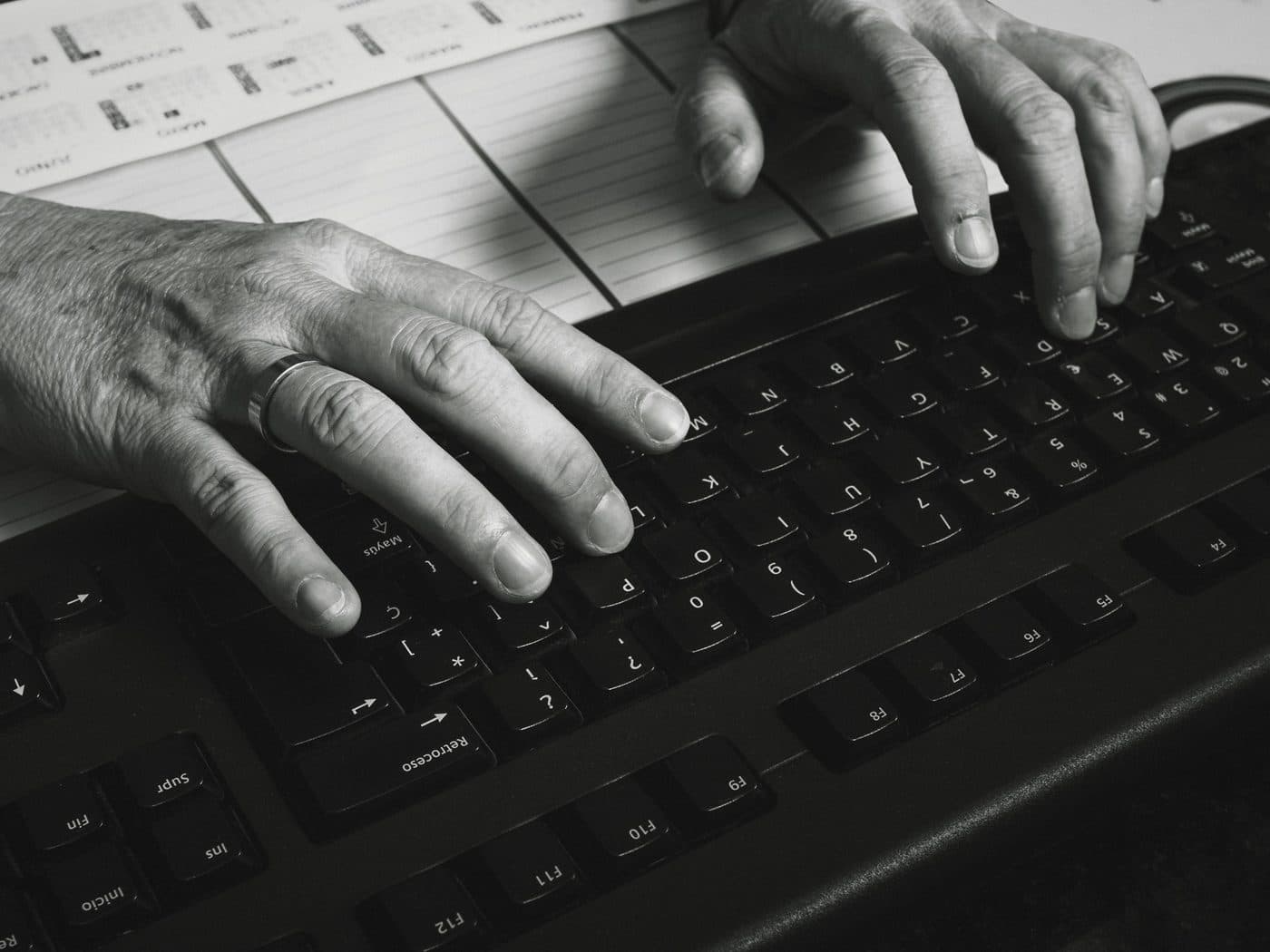 Hands typing on a black keyboard beside a printed calendar.